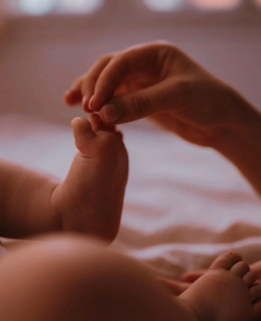 Une main d'adulte effleure le pied d'un bébé allongé, en réflexologie affective